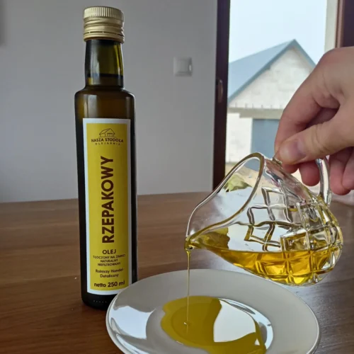 Olej rzepakowy Nasza Stodoła nalewany z karafki na talerzyk, obok stoi butelka z etykietą produktu